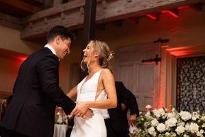 A couple shares their first dance at their wedding reception under ambient lighting.