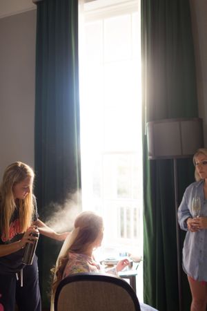 Hair styling session in progress near a window with sunlight streaming through green curtains.
