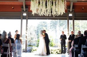 Wedding ceremony under a white floral chandelier with guests seated in rows.