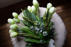 An elegant white tulip bouquet with delicate greenery and baby's breath arranged on a dark wooden surface.