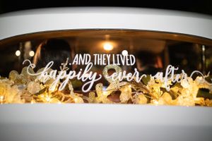 Wedding sign reading 'And they lived happily ever after' illuminated with string lights.