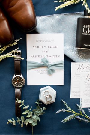 Elegant wedding invitation with blue ribbon displayed with accessories on navy background.