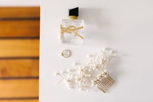 Wedding accessories including perfume, hair comb and rings arranged on wooden surface.