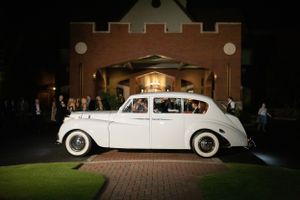 Classic white vintage Rolls Royce parked outside a brick building at night.