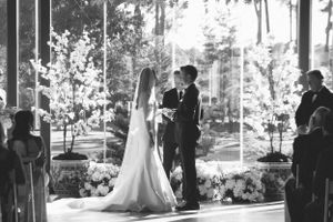 Wedding ceremony taking place in an elegant venue with large windows and natural light.