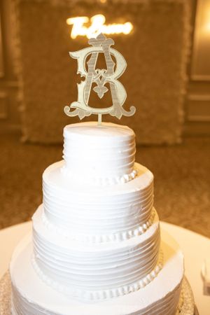Elegant white wedding cake with ornate monogram topper decoration.