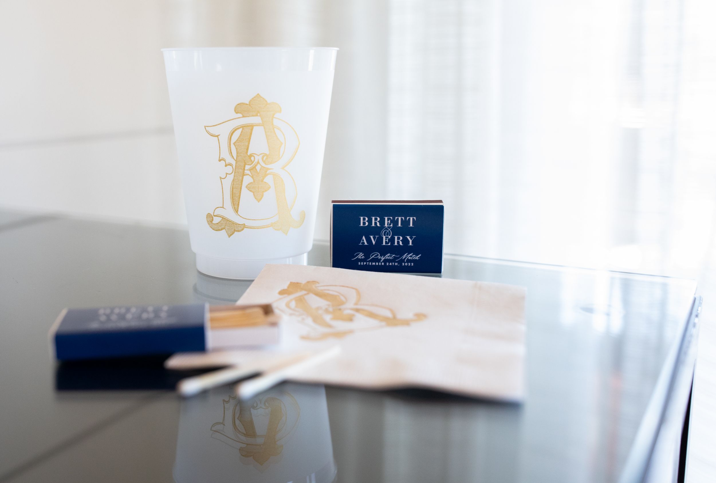 Wedding details featuring navy and gold monogrammed items on a reflective surface.