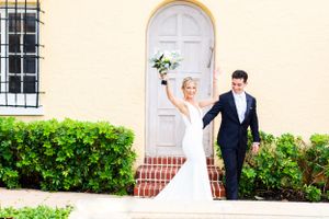 Joyful newlyweds celebrate outside a Mediterranean-style building with white door.
