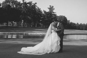 A black and white wedding photo captured on a golf course near a pond at sunset.