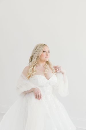 A romantic bridal portrait against a white backdrop showcasing a flowing wedding gown.