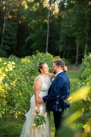 A romantic wedding couple embraces in a lush vineyard garden at sunset.