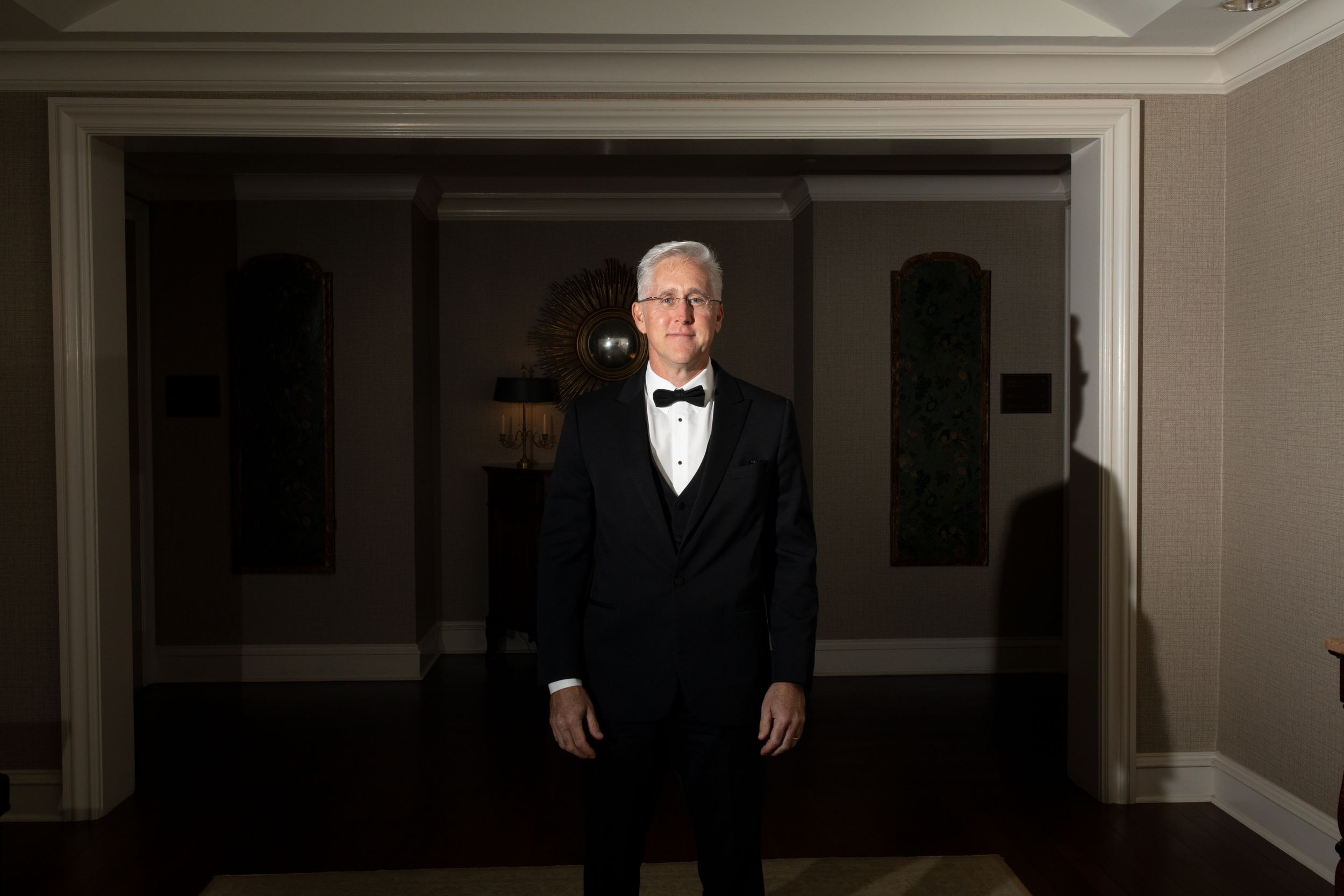 Wedding party member stands in formal attire in an elegant hallway.