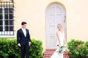 Wedding couple poses by arched white door and garden entrance.