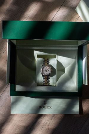 Luxury Rolex watch displayed in an elegant green presentation box with dramatic lighting.