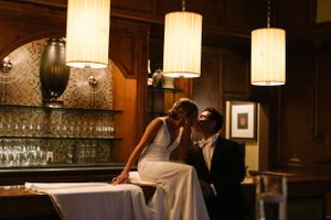 An intimate moment captured in warm lighting at an elegant bar setting with pendant lamps.