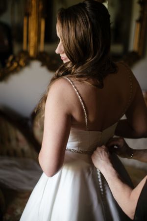 A white wedding dress being buttoned up from behind, showcasing delicate beaded straps and elegant fabric.