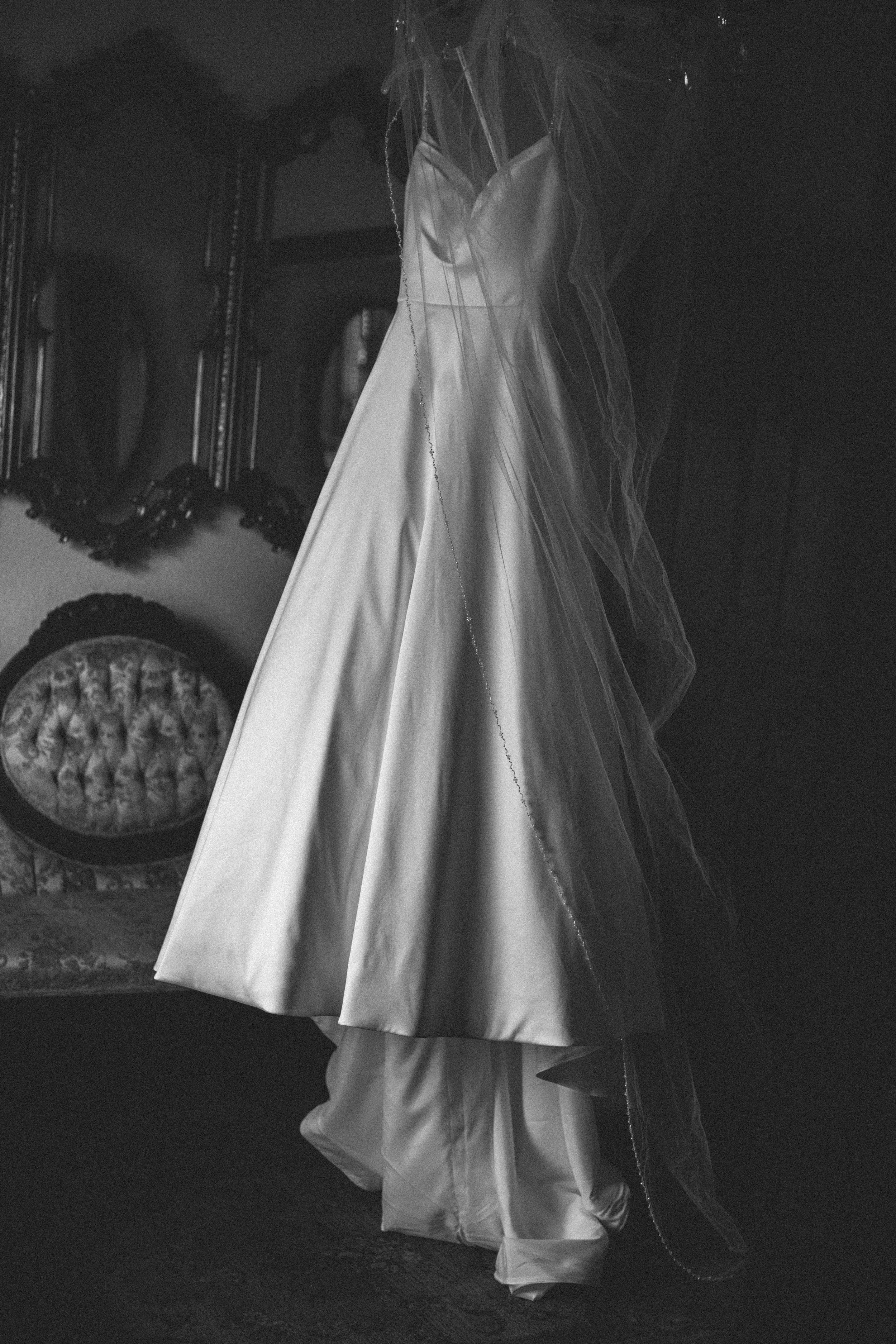 Classic white wedding gown displayed against dark wall with vintage furniture.