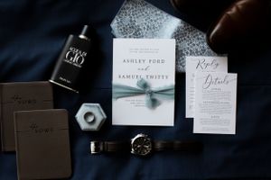 Wedding stationery and accessories arranged on dark blue fabric with modern design elements.