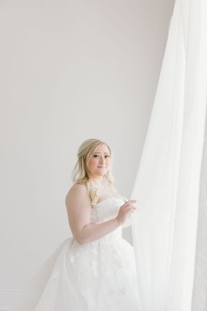 A bridal portrait in a white room next to sheer curtains with soft natural lighting.