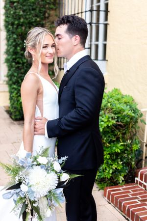 A white wedding bouquet with blue accents complements an elegant bridal portrait against ivy-covered walls.