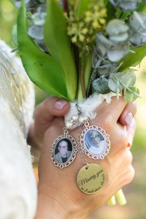 A hand holding a bridal bouquet with vintage photo charms attached featuring memorial photos.