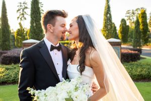 Sunset wedding portrait with white bouquet and flowing veil in a formal garden.