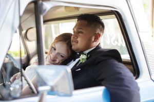 Happy couple smiling together in the front seat of a classic car on their wedding day.