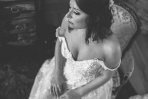 Black and white portrait of bride in lace off-shoulder wedding gown.