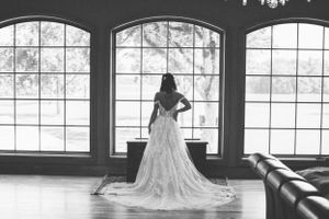 Silhouette by arched windows shows dramatic train of wedding gown in black and white.