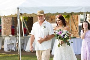 Wedding couple walking outdoors past white reception tables and stone wall.