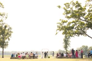 Wide landscape shot of wedding guests gathered under trees during an outdoor celebration.