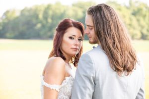 Romantic couple portrait in formal attire against a sunlit field background.