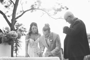 Black and white ceremony photo of people signing documents during an outdoor wedding.
