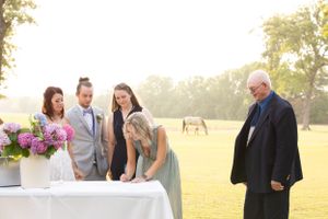 Wedding guests gather around signing table in outdoor sunlit setting.