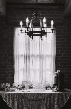 A black and white photo of an elegant chandelier over a table with white curtains and linens.