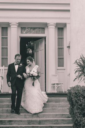 A black and white photo of a couple descending white columned stairs at a historic venue.