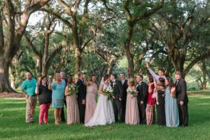 A wedding party gathered under moss-draped oak trees in an outdoor setting.
