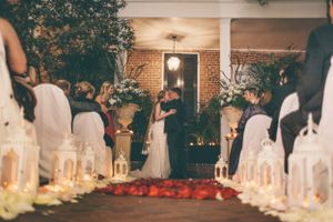 A candlelit wedding ceremony aisle decorated with lanterns and rose petals leading to a brick backdrop.