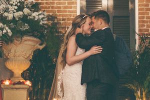 A romantic wedding portrait with the couple embracing near a brick wall adorned with floral arrangements.