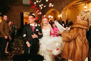 Wedding party exits venue amid floating feathers and festive lighting.