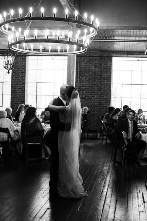 First dance at wedding reception under circular chandelier in rustic venue.