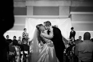 A black and white photo of newlyweds sharing their first dance surrounded by wedding guests.