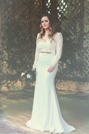Modern two-piece wedding dress with lace top and flowing skirt against garden lattice background.