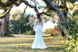 Bride in fitted lace wedding dress poses under majestic oak trees at sunset.
