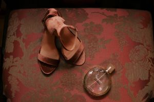 Pink sandals and perfume bottle arranged on floral patterned surface.