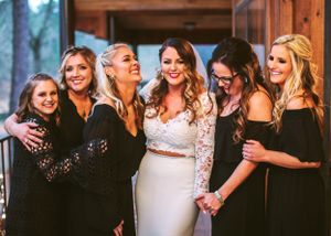 A group of bridesmaids in black dresses share a joyful moment with the bride in white at a wedding celebration.