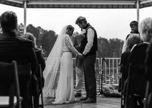 Black and white photo of a couple exchanging vows during an outdoor wedding ceremony.