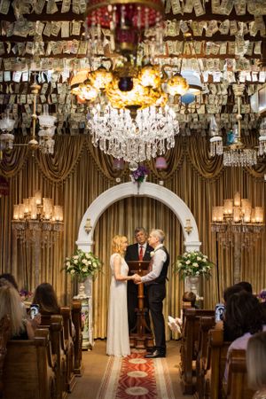 Wedding ceremony in elegant chapel with crystal chandeliers and gold drapery.