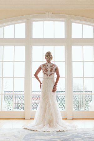 Back view of lace wedding dress silhouetted against large arched windows.