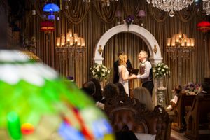 A wedding ceremony under an arched altar with chandeliers and dramatic drapery in warm lighting.
